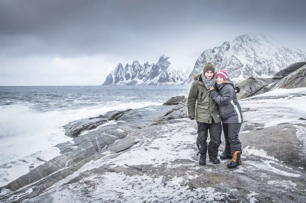 Couple sur les rochers face aux sommets de l'île de Senja en hiver